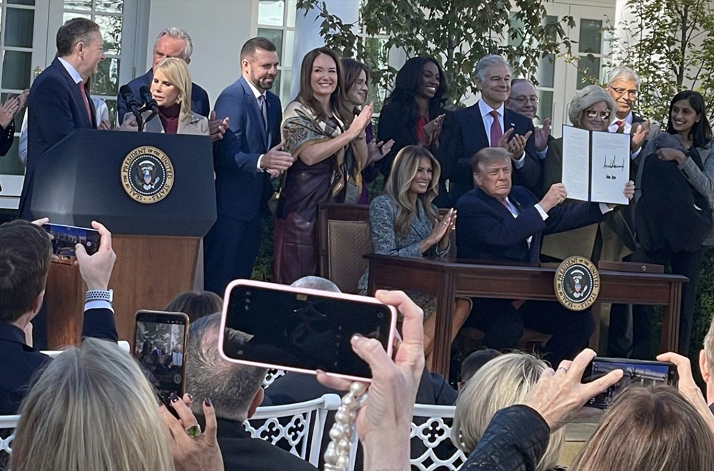 President Trump holds up his Executive Order for "Advancing Women's Health to Improve Outcomes in All Phases of Life," attended by Melania Trump and leaders in his administration.